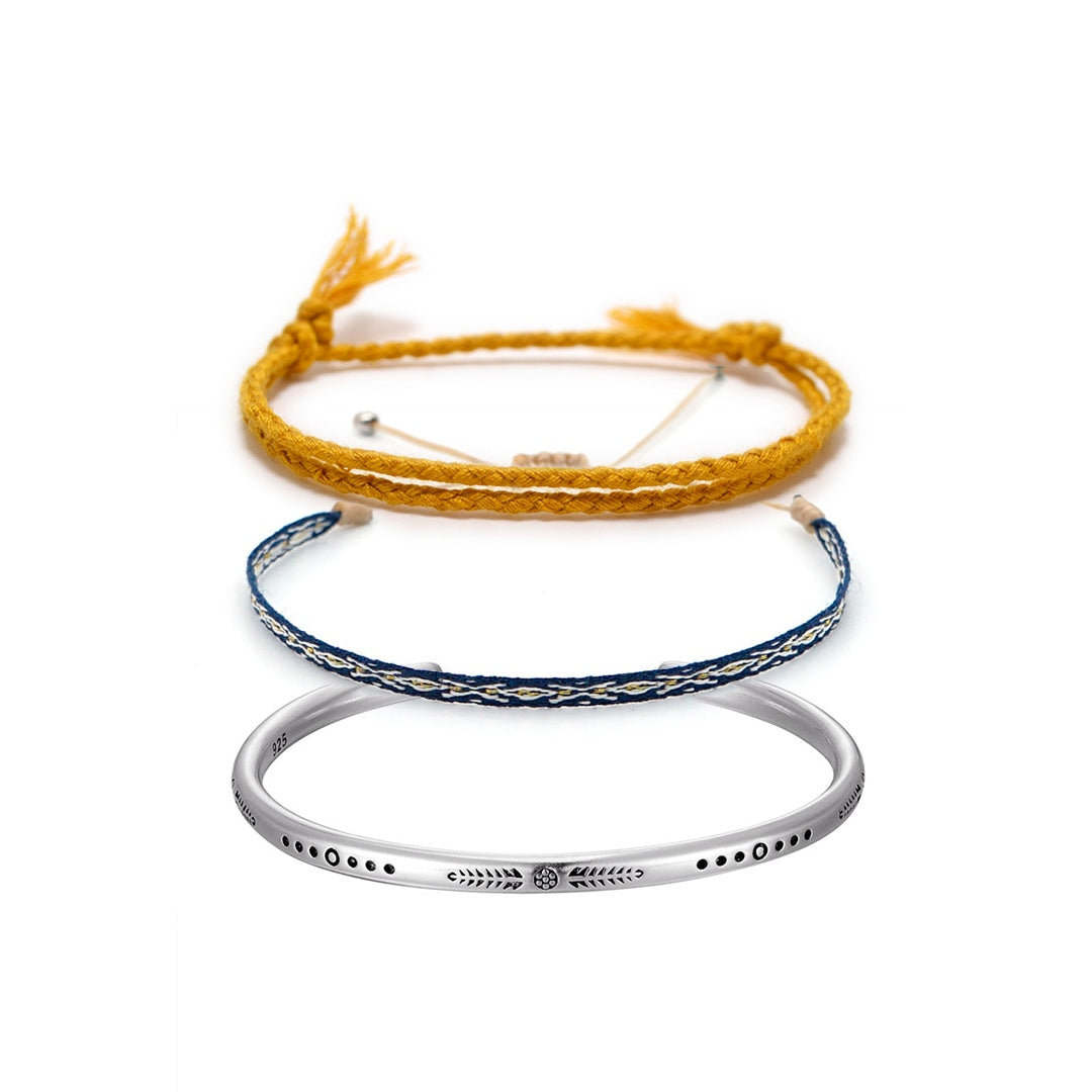 Conjunto budista com duas pulseiras, corda amarela e fio azul, e bracelete de prata tibetana gravado, simbolizando fé e proteção espiritual - Pelicano Azul