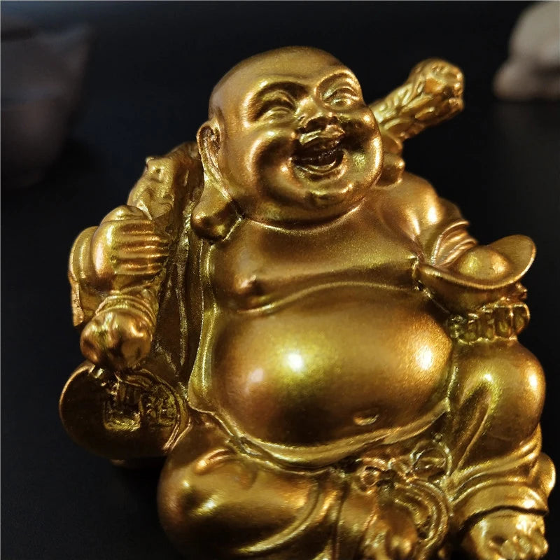 Estátua dourada do Buda Gordo Sorridente, segurando um lingote e um saco de fortuna, simbolizando alegria e prosperidade. Pelicano Azul.