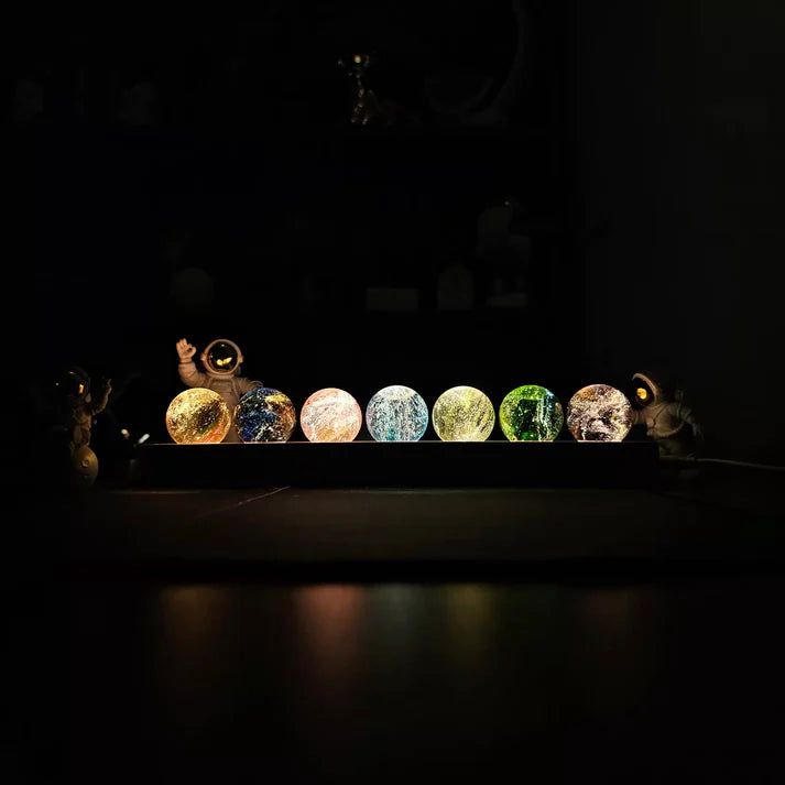 luminária decorativa com sete esferas coloridas dos chakras iluminadas e astronautas ao lado.