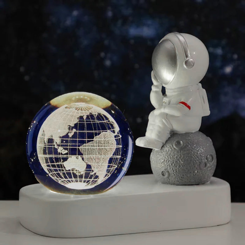 Luminária decorativa de astronauta sentado na Lua ao lado de um globo terrestre iluminado, perfeita para ambientes temáticos.