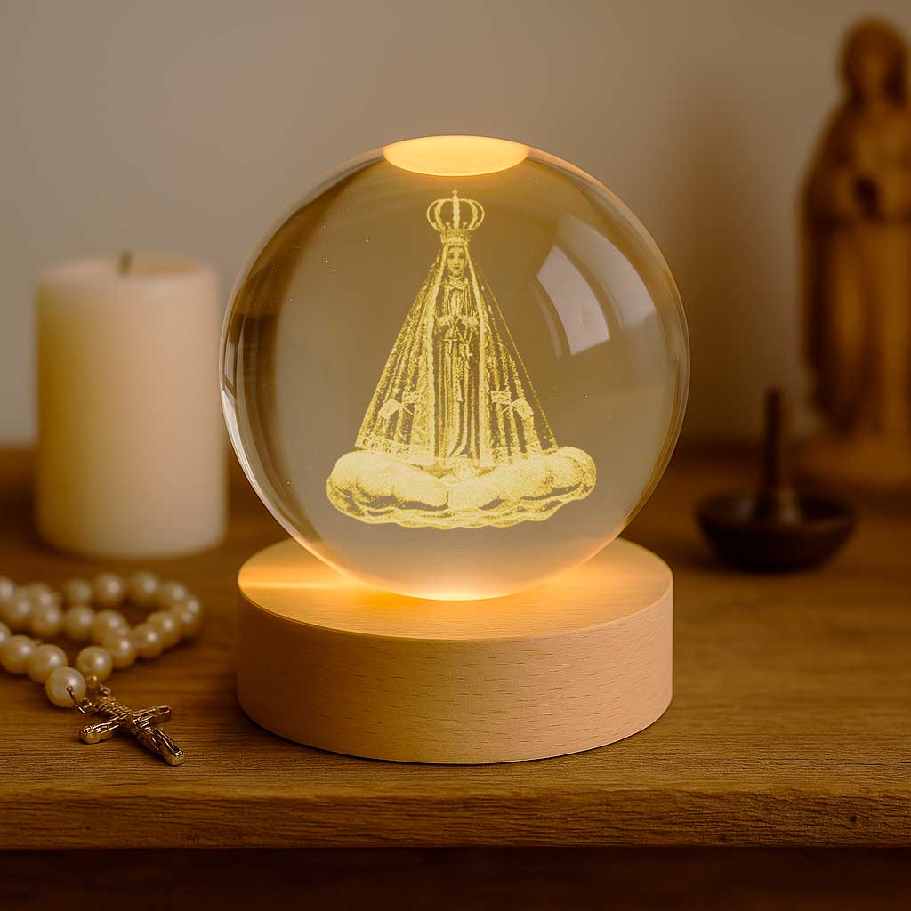 Luminária com imagem de santa em esfera de vidro iluminada sobre base de madeira clara.