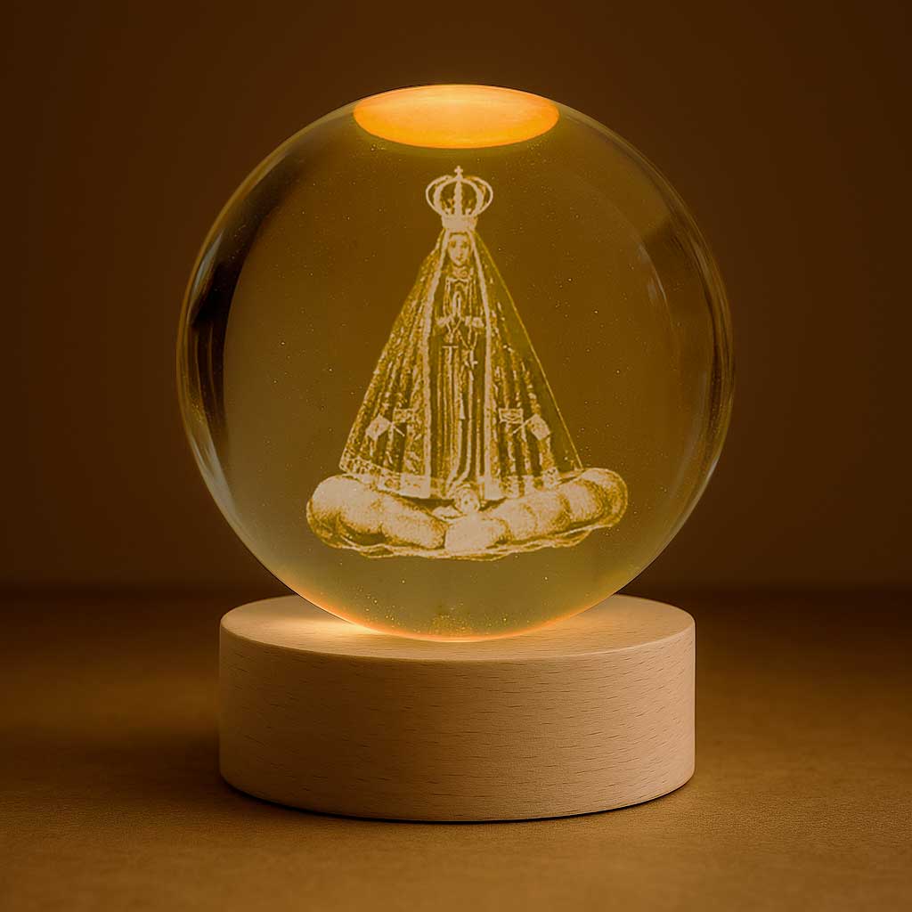 Luminária com santa entalhada em esfera de vidro iluminada, sobre base de madeira clara.