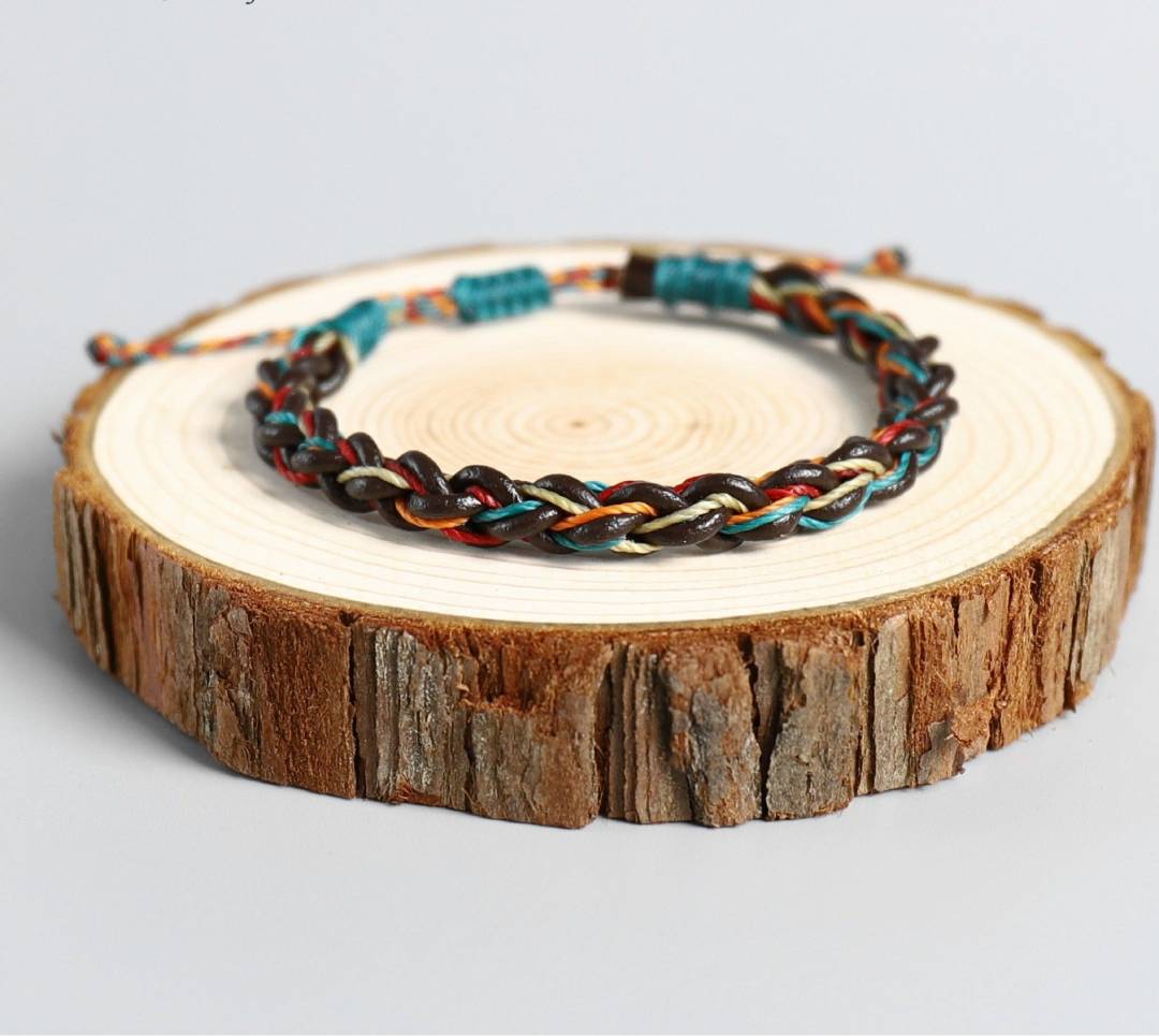 Pulseira Budista Macramê Multicolor sobre base de madeira cortada, cores vibrantes em padrão trançado, Pelicano Azul.