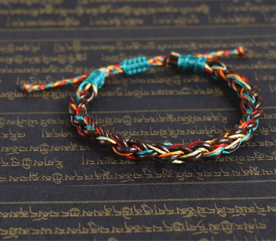Pulseira Budista Macramê Multicolor sobre escrita tibetana em fundo preto, Pelicano Azul.