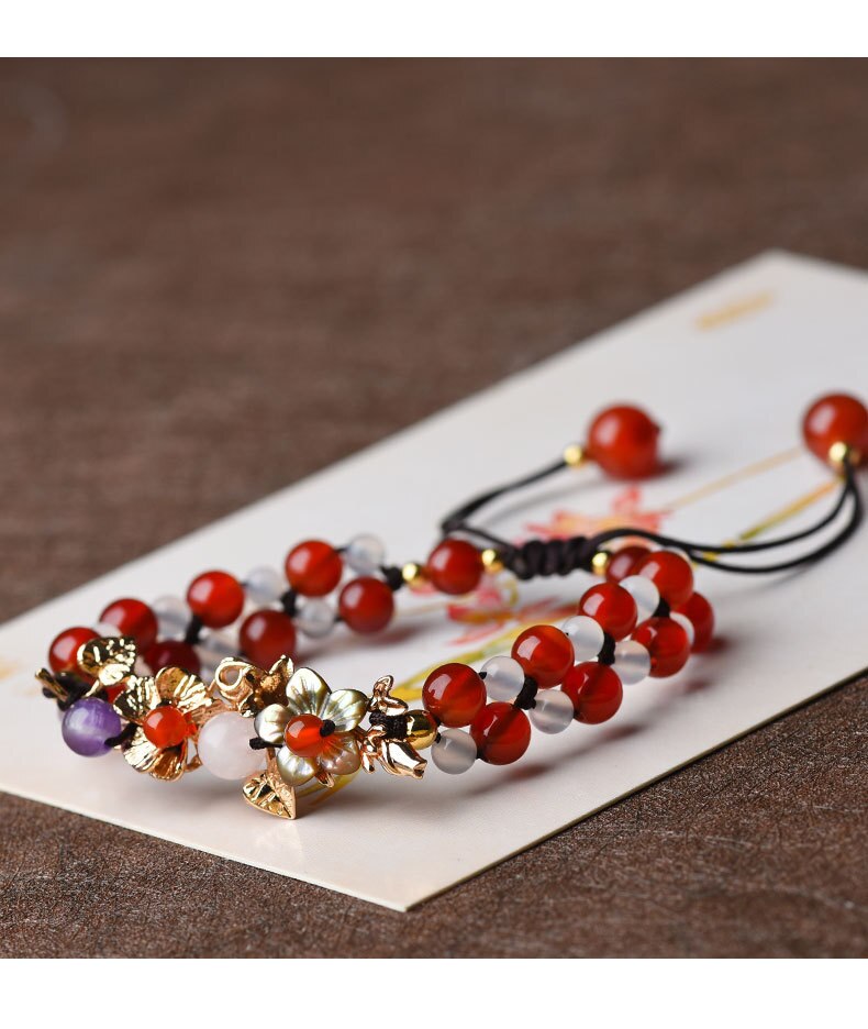 Pulseira Flores de Jade com detalhes florais em metal dourado, composta por contas vermelhas e translúcidas, trazendo um toque delicado e sofisticado - Pelicano Azul.