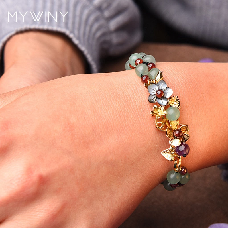 Pulseira Flores de Jade sendo usada no pulso, exibindo suas contas verdes e detalhes florais dourados, que adicionam um toque elegante e natural - Pelicano Azul.