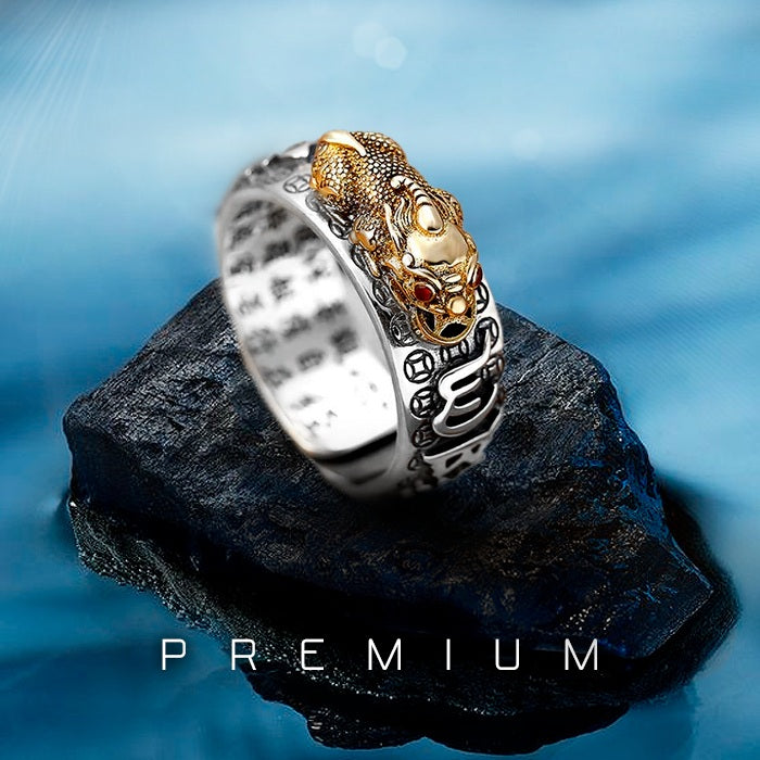 Anel Feng Shui prateado com símbolo de Pixiu dourado em relevo, decorado com mantras e detalhes orientais, Pelicano Azul.