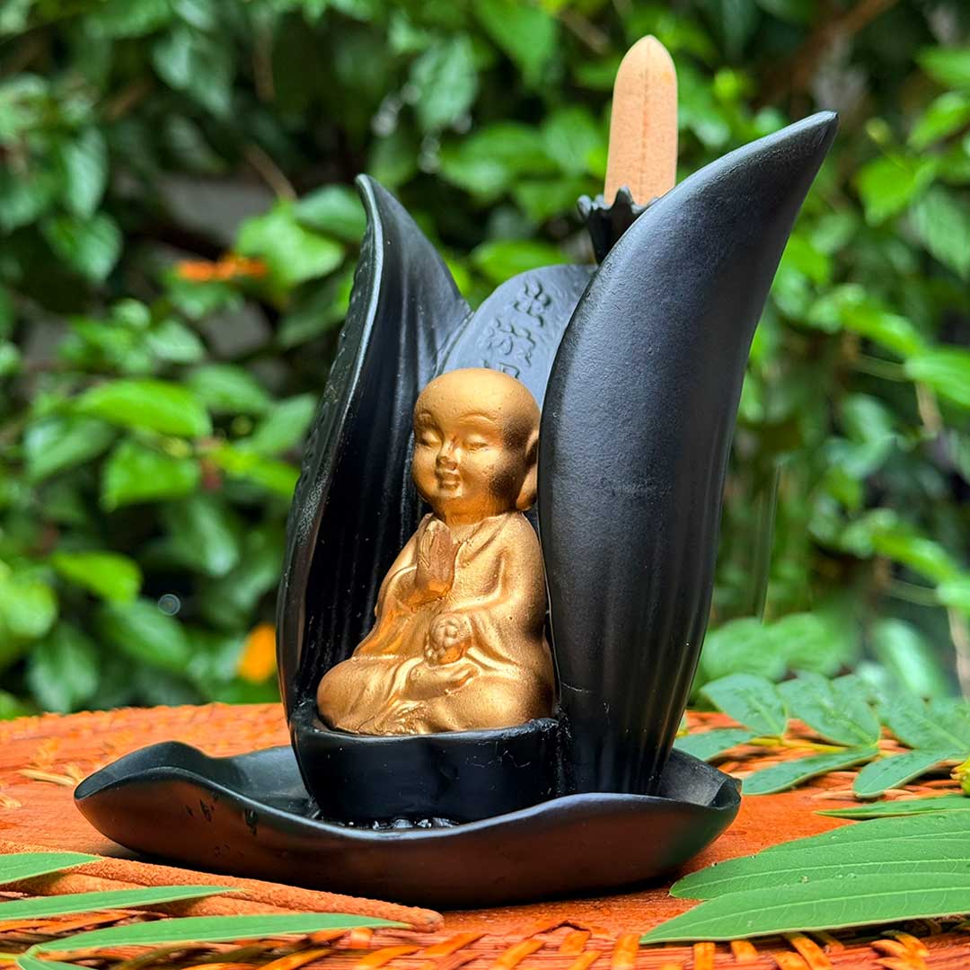 Incensário Lótus de Buda Pelicano Azul, peça em cerâmica preta com estátua dourada de Buda em prece.
