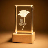 Luminária com flor 3D iluminada em bloco de cristal sobre base de madeira clara - Pelicano Azul