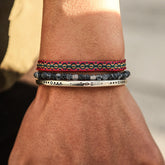 Três pulseiras budistas no pulso, incluindo uma pulseira colorida, contas de pedra e bracelete em prata tibetana.