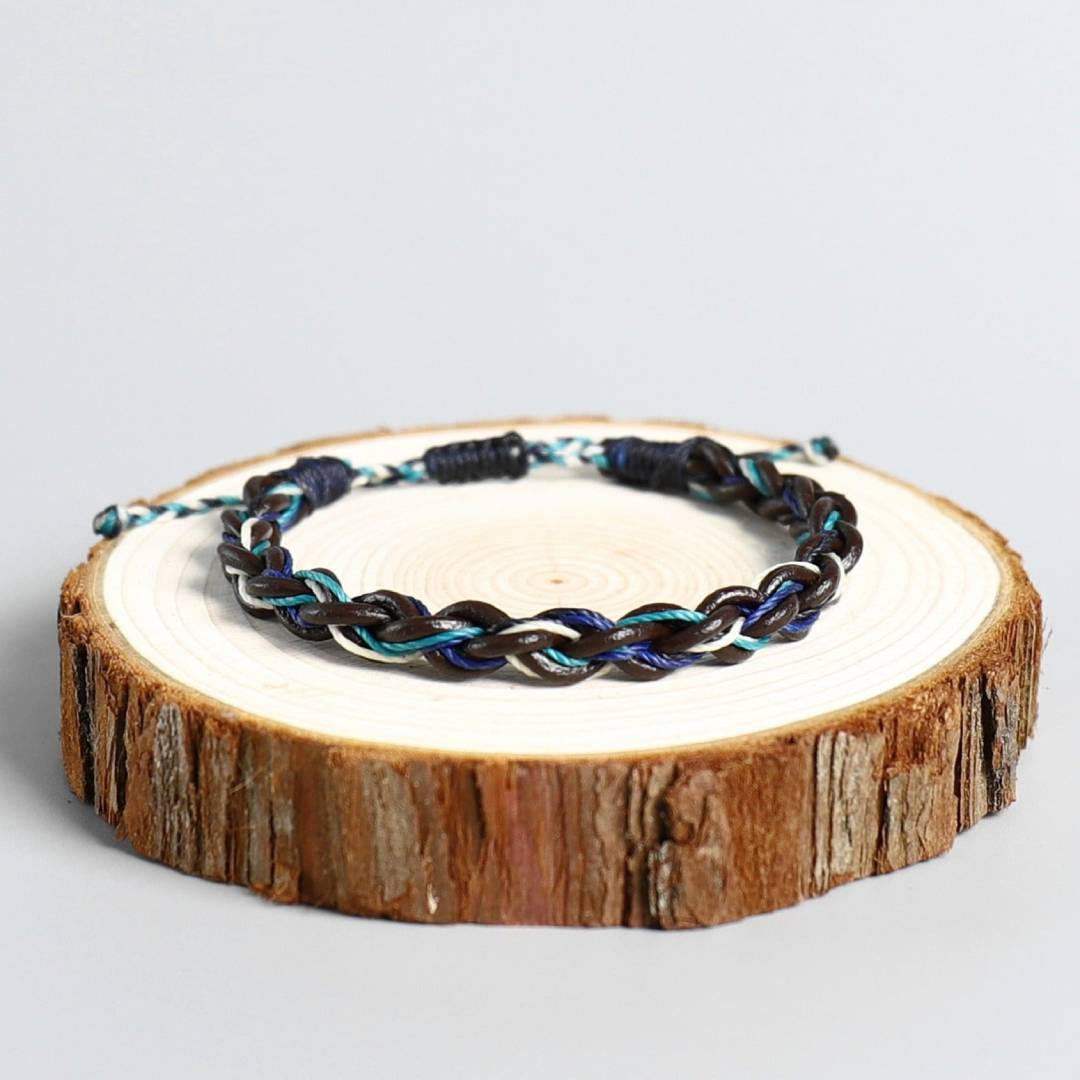 Pulseira Budista Macramê Multicolor trançada com fios azuis e pretos sobre base de tronco de madeira, Pelicano Azul.