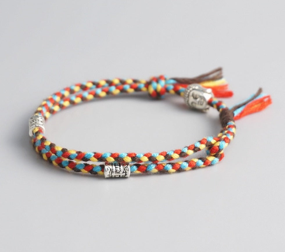 Pulseira Budista trançada em fios multicoloridos, com detalhes prateados de Buda e símbolos espirituais. Pelicano Azul.