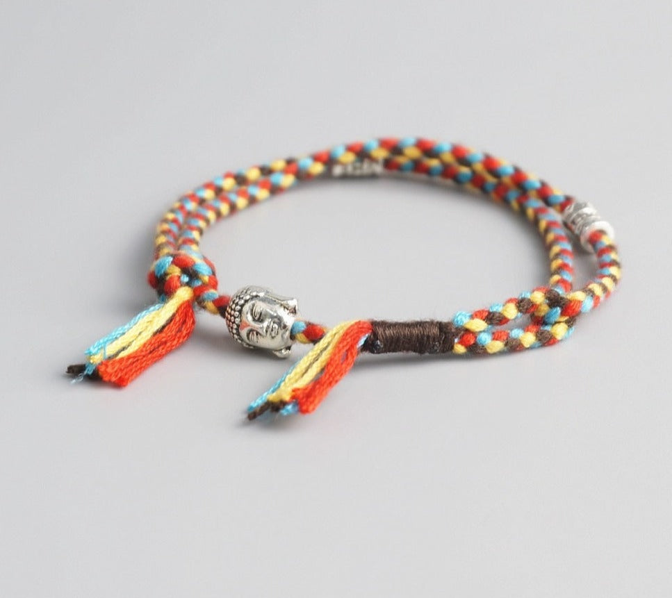 Pulseira Budista trançada em fios multicoloridos com detalhe de pingente prateado de Buda e franjas coloridas. Pelicano Azul.